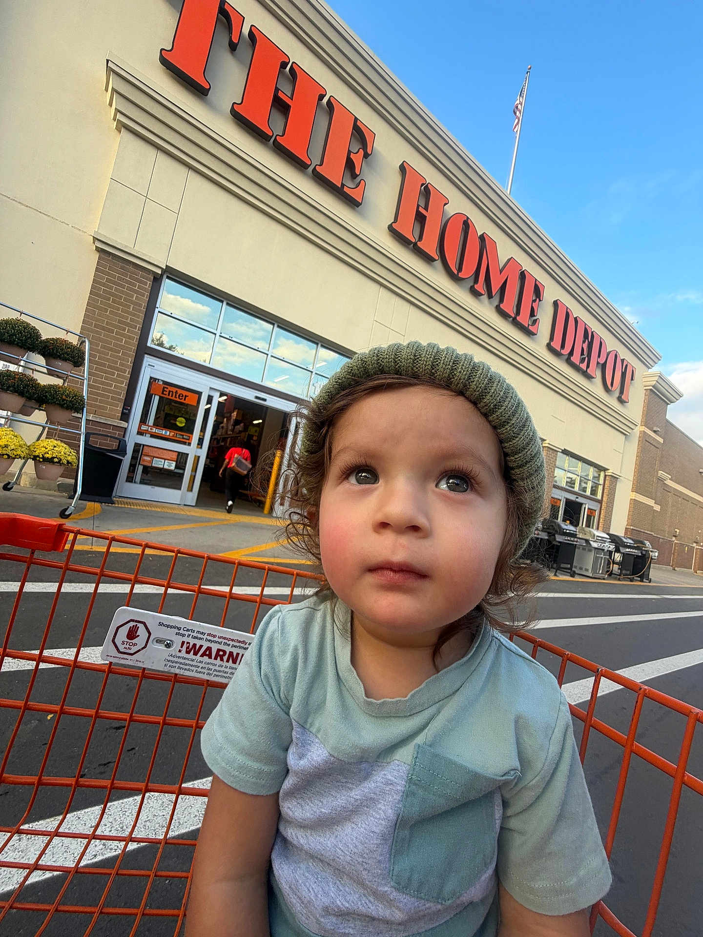 Eithan is registered to the contest to win money with this photo: beanie, building, casual_clothing, child, curious, curly_hair, daytime, face, home_depot, orange, outdoor, person, portrait, retail, shopping_cart, sky, storefront, street, toddler, young_child