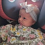 baby, car_seat, blanket, bow, child, infant, face, headband, clothing, seat, warning_label, portrait, cute, indoors, young_child, person, child_seat, soft_lighting, floral_pattern, safety