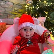 Paul participe au concours pour gagner de l'argent avec cette photo : baby, child, red_hat, red_outfit, christmas_tree, holiday_decor, gold_ribbon, glowing_light, cozy_chair, smiling, festive, indoor, holiday, cute, celebration, happy, portrait, seasonal, knit_hat, decorations