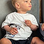toddler, child, mickey_mouse, tshirt, black_shorts, sneakers, shoe, couch, gray_couch, seated, side_profile, short_hair, casual_clothing, indoors, young_child, looking_away, small_chip, hand_visible, light_skin, curious_expression
