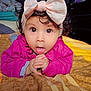 baby, child, pink_bow, headband, wide_eyes, curly_hair, blanket, indoor, cute, portrait, infant, expression, hands, clothing, lying_down, face, adorable, young_child, bedroom, curiosity