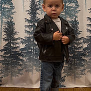 Marcus joined the competition — help win amazing prizes! toddler, child, leather_jacket, jeans, barefoot, wooden_floor, forest_backdrop, indoor, portrait, standing, cute, serious_expression, young, person, fashion, casual, small, clothing, background, floor