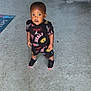 toddler, child, concrete, floor, stairs, clothing, sneakers, curious, standing, looking_up, outdoor, doormat, black, red, yellow, patterned, young_child, person, casual, daylight