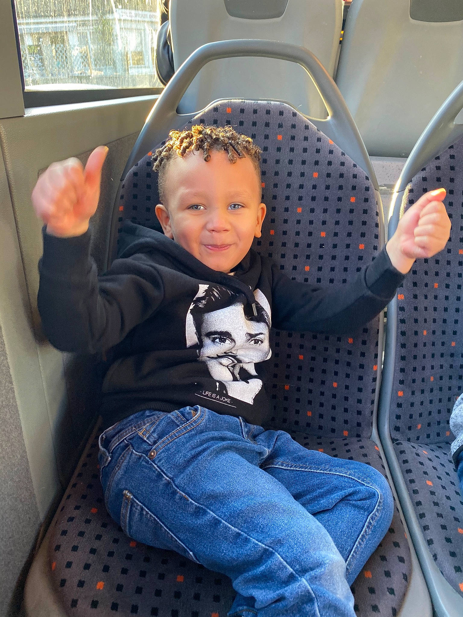 Jean Elie a rejoint le concours — aidez-le/la à gagner de superbes lots ! auto_part, baby, baby_in_car_seat, car, car_seat, child, finger, jeans, luxury_vehicle, person, sitting, steering_wheel, toddler, vacation, vehicle, vehicle_door