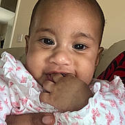 Oripa is registered to the contest to win money with this photo: baby, child, infant, face, hand, fingers, clothing, floral_pattern, indoor, person, cute, portrait, skin, expression, sitting, adult_hand, young_child, closeup, smiling, wearing