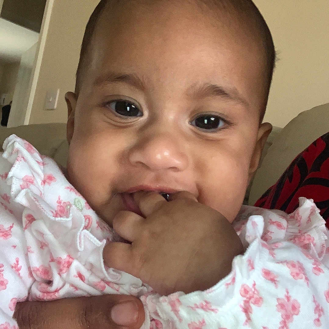 Oripa is registered to the contest to win money with this photo: adult_hand, baby, child, closeup, clothing, cute, expression, face, fingers, floral_pattern, hand, indoor, infant, person, portrait, sitting, skin, smiling, wearing, young_child