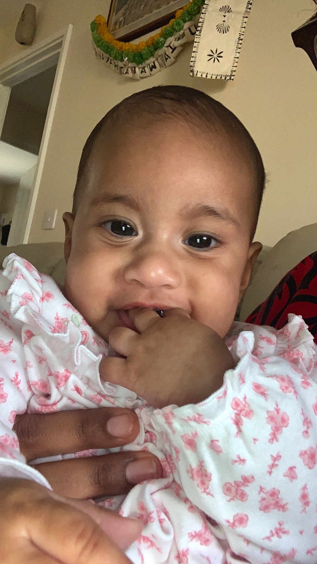 Oripa is registered to the contest to win money with this photo: baby, child, infant, face, hand, fingers, clothing, floral_pattern, indoor, person, cute, portrait, skin, expression, sitting, adult_hand, young_child, closeup, smiling, wearing