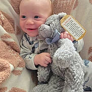 Callum is registered to the contest to win money with this photo: baby, infant, smile, blanket, stuffed_animal, plush_toy, elephant, pajamas, hand, tag, bow, face, eyes, newborn, cozy, portrait, soft_texture, nursery, cuddle, happy