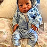 baby, infant, blue_clothing, hoodie, pants, socks, sitting, cushion, floral_pattern, tiger_pattern, indoor, face, curious_expression, newborn, hands, blanket, soft_fabric, portrait, young_child, cozy