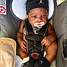 baby, infant, car_seat, pacifier, headband, black_clothing, socks, harness, seatbelt, child, cute, indoors, sitting, secure, closeup, young, person, portrait, curly_hair, warning_label