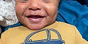 Braylin is registered to the contest to win money with this photo: baby, infant, child, smiling, happy, face, closeup, dimples, eyes, tooth, onesie, clothing, car_graphic, text_on_clothing, blanket, plush, blue_blanket, mustard_color, portrait, lying_down