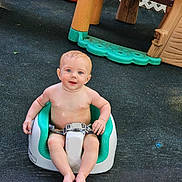 Owen is registered to the contest to win money with this photo: baby, child, seat, outdoor, playground, toy, smiling, happy, skin, bare_chest, hand, play_area, plastic, fence, foot, young_child, person, infant, sitting, daylight