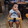 american_flag, baby, casual_clothing, chairs, child, curly_hair, cute, flooring, high_chair, indoor, menu, people_in_background, restaurant, sneakers, table, television, toddler, waiting, wooden_chair, wooden_furniture