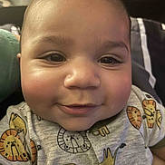 Kaleb joined the competition — help win amazing prizes! baby, infant, smiling, close_up, face, cheeks, eyes, onesie, lion_print, clothing, portrait, cute, expression, skin, head, indoor, bedding, pillow, toy, happy