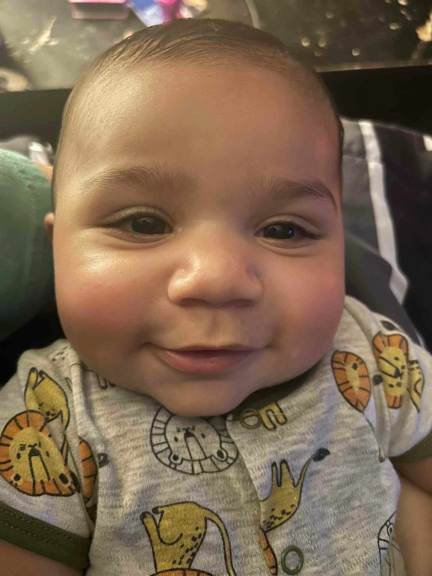 Kaleb joined the competition — help win amazing prizes! baby, infant, smiling, close_up, face, cheeks, eyes, onesie, lion_print, clothing, portrait, cute, expression, skin, head, indoor, bedding, pillow, toy, happy