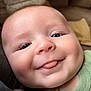 baby, close_up, face, tongue, cheeks, blue_eyes, green_clothing, pacifier_clip, smiling, cute, infant, child, indoors, soft_texture, blanket, happy, person, portrait, young_child, skin