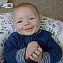 Finnley is registered to the contest to win money with this photo: baby, smiling, blue_clothing, cushion, carpet, indoor, face, hands, infant, person, cute, happy, comfortable, patterned, home, child, sitting, young, portrait, casual