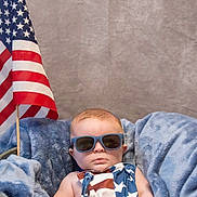 Finnley is registered to the contest to win money with this photo: american_flag, baby, blanket, blue, child, clothing, cute, face, flag, head, indoor, infant, patriotic, person, portrait, serious, stars, stripes, sunglasses, tub