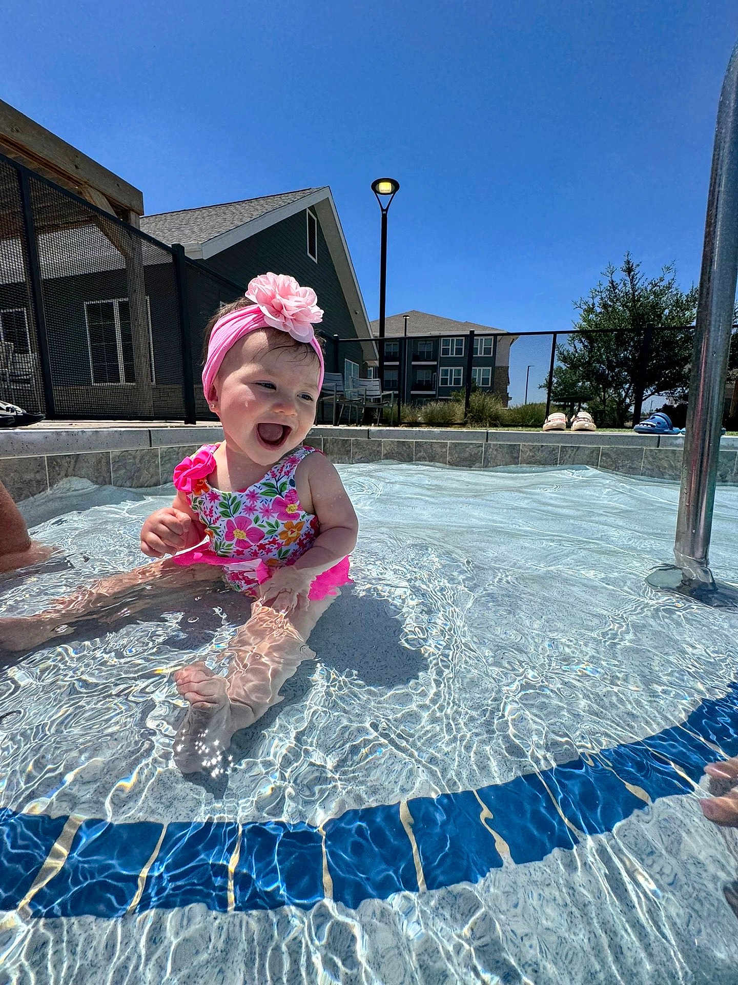 Roseily is registered to the contest to win money with this photo: baby, blue_sky, child, fence, flower, foot, happy, headband, outdoor, person, play, pool, residential, smiling, splashing, summer, sunny, swimsuit, water, water_reflection
