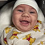 baby, smiling, infant, white_cap, winnie_the_pooh, onesie, cute, happy, face, child, portrait, closeup, cushion, indoor, soft_lighting, baby_clothes, young_child, expression, headwear, comfort