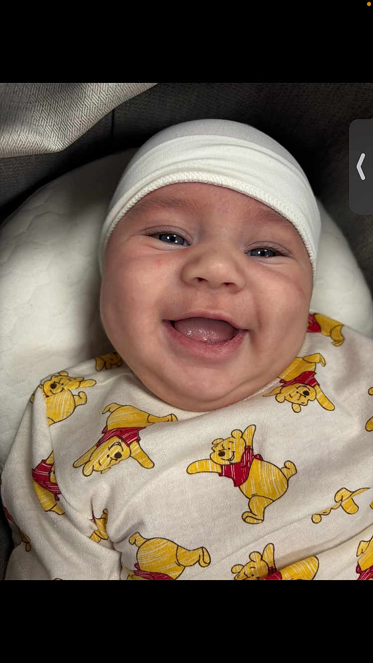 Dior is registered to the contest to win money with this photo: baby, smiling, infant, white_cap, winnie_the_pooh, onesie, cute, happy, face, child, portrait, closeup, cushion, indoor, soft_lighting, baby_clothes, young_child, expression, headwear, comfort
