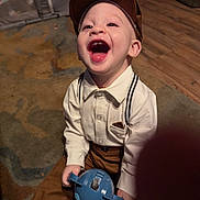 Huxley joined the competition — help win amazing prizes! child, toddler, laughing, indoor, carpet, toy, cap, suspenders, brown_pants, white_shirt, happy, person, floor, playing, cute, smiling, baby, clothing, headwear, portrait