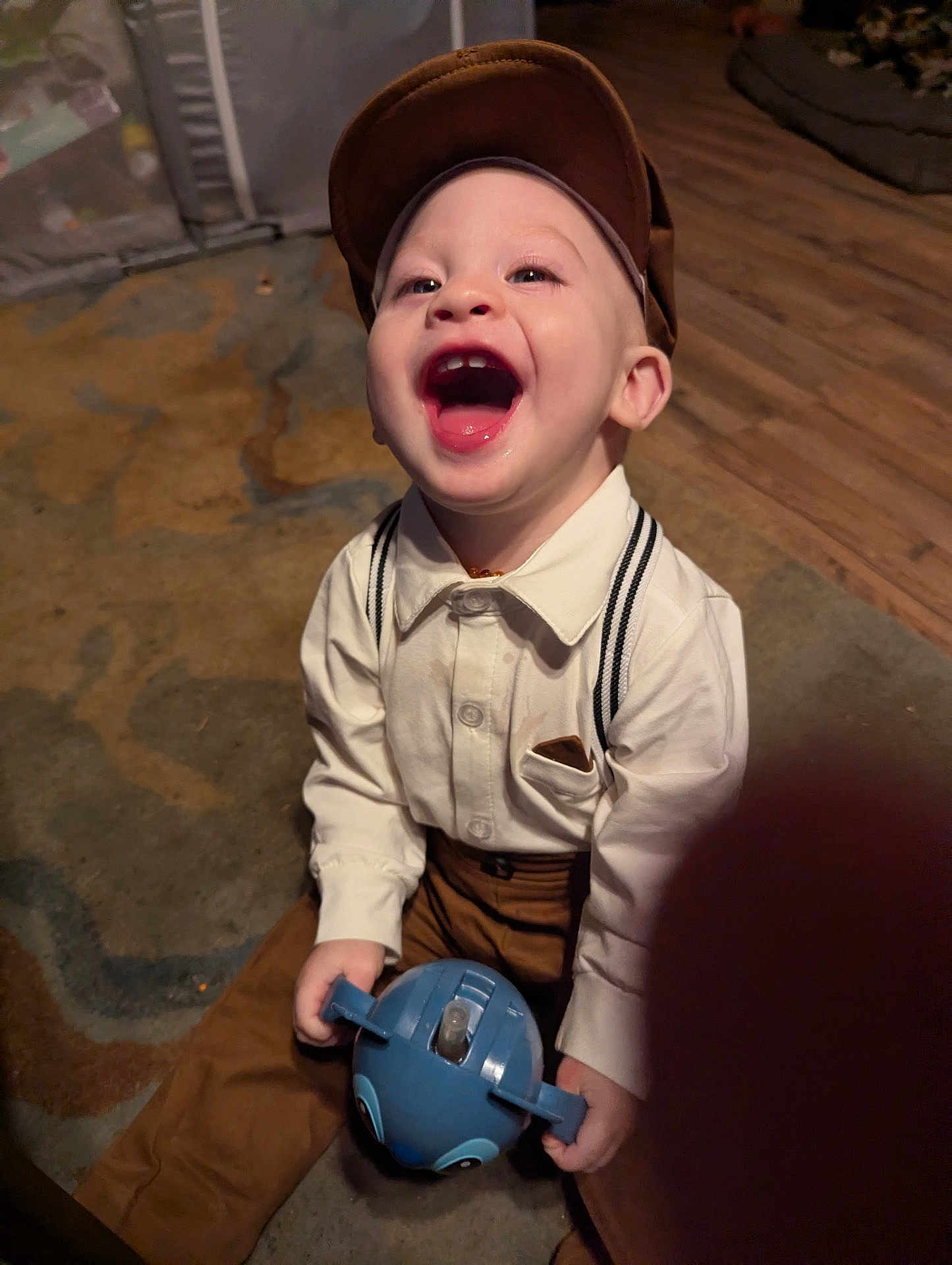 Huxley joined the competition — help win amazing prizes! child, toddler, laughing, indoor, carpet, toy, cap, suspenders, brown_pants, white_shirt, happy, person, floor, playing, cute, smiling, baby, clothing, headwear, portrait