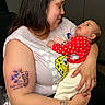 woman, baby, tattoo, arm, holding, red_clothing, polka_dot, indoor, smiling, face, person, love, mother, child, cute, skin, hair, long_hair, sitting, casual_clothing