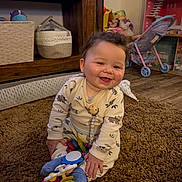 Tommy joined the competition — help win amazing prizes! baby, child, smiling, toys, carpet, indoor, wooden_shelf, toy_stroller, plush, clothing, floor, happy, person, cute, infant, playtime, room, home, sitting, pacifier_clip