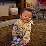 baby, child, smiling, toys, carpet, indoor, wooden_shelf, toy_stroller, plush, clothing, floor, happy, person, cute, infant, playtime, room, home, sitting, pacifier_clip