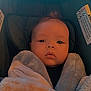 baby, blanket, face, infant, stroller, child, cozy, soft_texture, warm_lighting, wrapped, indoors, cute, young_child, head, seated, looking_at_camera, portrait, comfort, expressionless, bundle