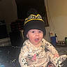 baby, infant, child, portrait, sitting, surprised, wide_eyed, open_mouth, beanie, pom_pom_hat, pajamas, patterned_clothing, indoor, home, flash_photography, furniture, cup, blanket, cozy, family_photo