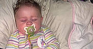 Kaylanna is registered to the contest to win money with this photo: baby, infant, sleeping, pacifier, striped_clothing, onesie, pink, blanket, pillow, bed, toy, portrait, indoors, cozy, curly_hair, closed_eyes, sitting, relaxed, household_items, nursery