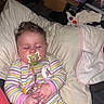 baby, infant, sleeping, pacifier, striped_clothing, onesie, pink, blanket, pillow, bed, toy, portrait, indoors, cozy, curly_hair, closed_eyes, sitting, relaxed, household_items, nursery