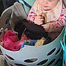 Kaylanna is registered to the contest to win money with this photo: baby, child, infant, laundry_basket, laundry, clothing, sitting, indoors, portrait, face, smiling, curly_hair, bib, pink_clothing, colorful, household, basket, playful, home, candid