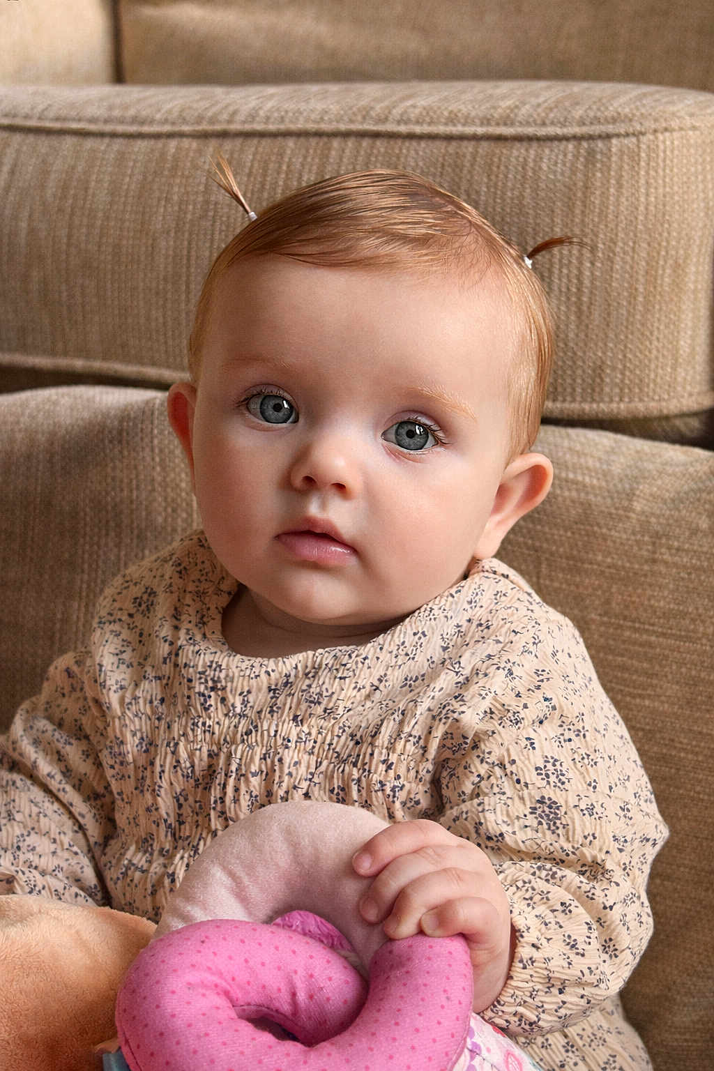 Navie Grace is registered to the contest to win money with this photo: baby, infant, child, portrait, blue_eyes, pink_toy, plush_toy, sofa, indoors, pigtails, patterned_dress, hand, face, skin, eyelashes, gaze, cute, soft_lighting, seated, closeup