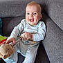 baby, smile, dimples, plush_toy, striped_pajamas, couch, gray_furniture, happy, child, indoors, cute, person, sitting, toy, infant, playful, face, hand, feet, light