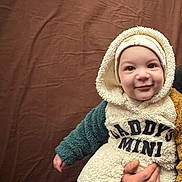 ümit a rejoint le concours — aidez-le/la à gagner de superbes lots ! baby, child, infant, hooded_clothing, fluffy_outfit, socks, bear_face_socks, smiling, person, cute, indoor, brown_background, hand, warm_clothing, portrait, baby_wear, adorable, young_child, happy, cozy