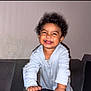 toddler, child, smiling, curly_hair, indoor, couch, happy, person, baby_clothes, face, home, furniture, joy, portrait, leaning, cute, young_child, light_skin, playful, expression