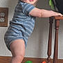 baby, child, standing, onesie, striped_clothing, wooden_floor, wooden_table, toy, green_toy, orange_toy, knitted_blanket, indoor, smiling, happy, face, feet, hand, plant, wall_outlet, home