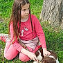 child, girl, puppy, dog, grass, tree, stick, outdoor, nature, pet, playing, pink_clothing, braided_hair, casual, young, animal, friendship, grass_field, sitting, daylight