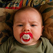 Patrick Froman is registered to the contest to win money with this photo: baby, infant, child, face, portrait, close_up, pacifier, red_pacifier, wide_eyed, eyes, smiling, couch, blanket, cushion, green_clothing, indoor, cozy, head, sitting, photograph