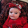baby, infant, child, headband, red_clothing, patterned_seat, face, portrait, cute, smile, indoor, person, young_child, sitting, closeup, apparel, headwear, happy, baby_seat, expression