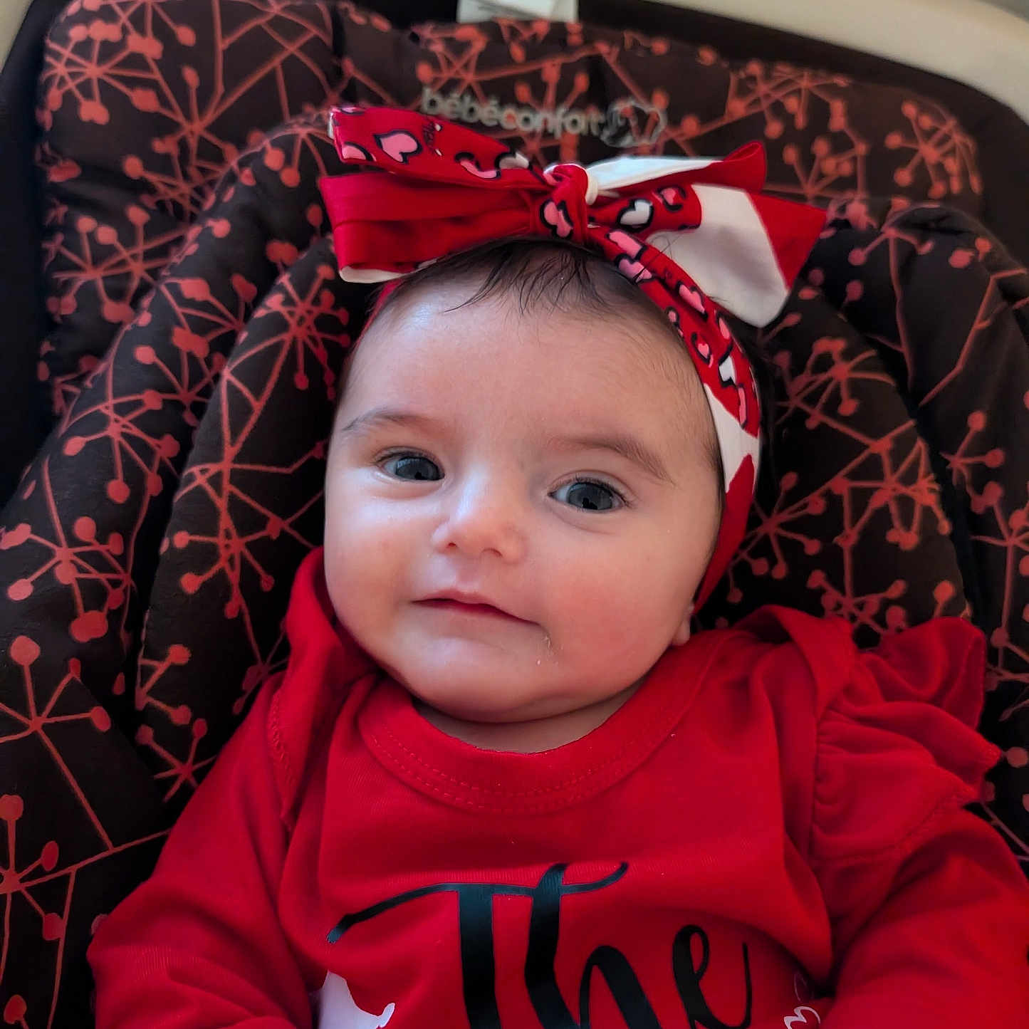 Eloyse a rejoint le concours — aidez-le/la à gagner de superbes lots ! apparel, baby, baby_seat, child, closeup, cute, expression, face, happy, headband, headwear, indoor, infant, patterned_seat, person, portrait, red_clothing, sitting, smile, young_child