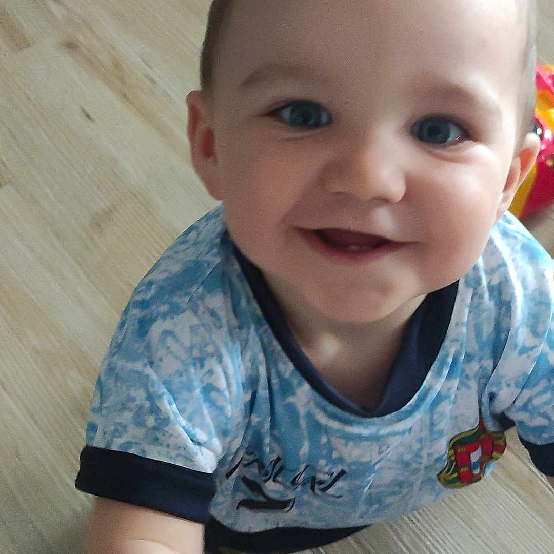 Lysio a rejoint le concours — aidez-le/la à gagner de superbes lots ! baby, blue_eyes, blue_shirt, bright, casual, cheerful, child, close_up, cute, happy, indoor, patterned_clothing, person, portrait, reaching, short_hair, smiling, toddler, wooden_floor, young_child