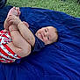 baby, child, grass, blanket, blue_blanket, outdoor, stroller, wheel, infant, cute, holding_feet, playing, smiling, happy, relaxed, casual_clothing, red_shorts, stars_pattern, person, nature