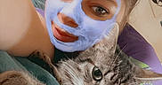 Demon a rejoint le concours — aidez-le/la à gagner de superbes lots ! person, cat, tabby_cat, facial_mask, face, flower, pink_flower, blanket, cozy, indoor, wall_art, tattoo, closeup, relaxed, snuggling, bedroom, purple_shirt, feline, pet, cute