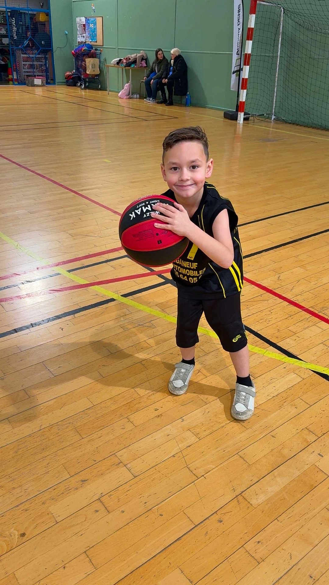 Diego a rejoint le concours — aidez-le/la à gagner de superbes lots ! bags, ball, basketball, bench, boy, child, court_lines, goal_net, gymnasium, hardwood_floor, indoor, portrait, shadow, smile, sneakers, spectators, sports_uniform, team, wall, wood_floor