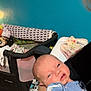Lilly is registered to the contest to win money with this photo: baby, newborn, infant, person, arm, clothing, blue_outfit, floral_pattern, blanket, bed, indoor, room, wall, teal_wall, baby_gear, crib, blanket_pattern, sleepy, holding, soft