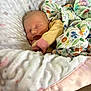 baby, newborn, sleeping, blanket, floral_pattern, soft, cushion, baby_nest, pastel_colors, cozy, infant, clothing, peaceful, indoors, resting, cute, face, child, comfort, wrapped
